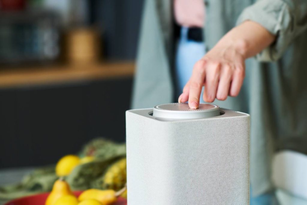 Close-up of young woman turning on smart speaker to listen to music while preparing food in the kitchen